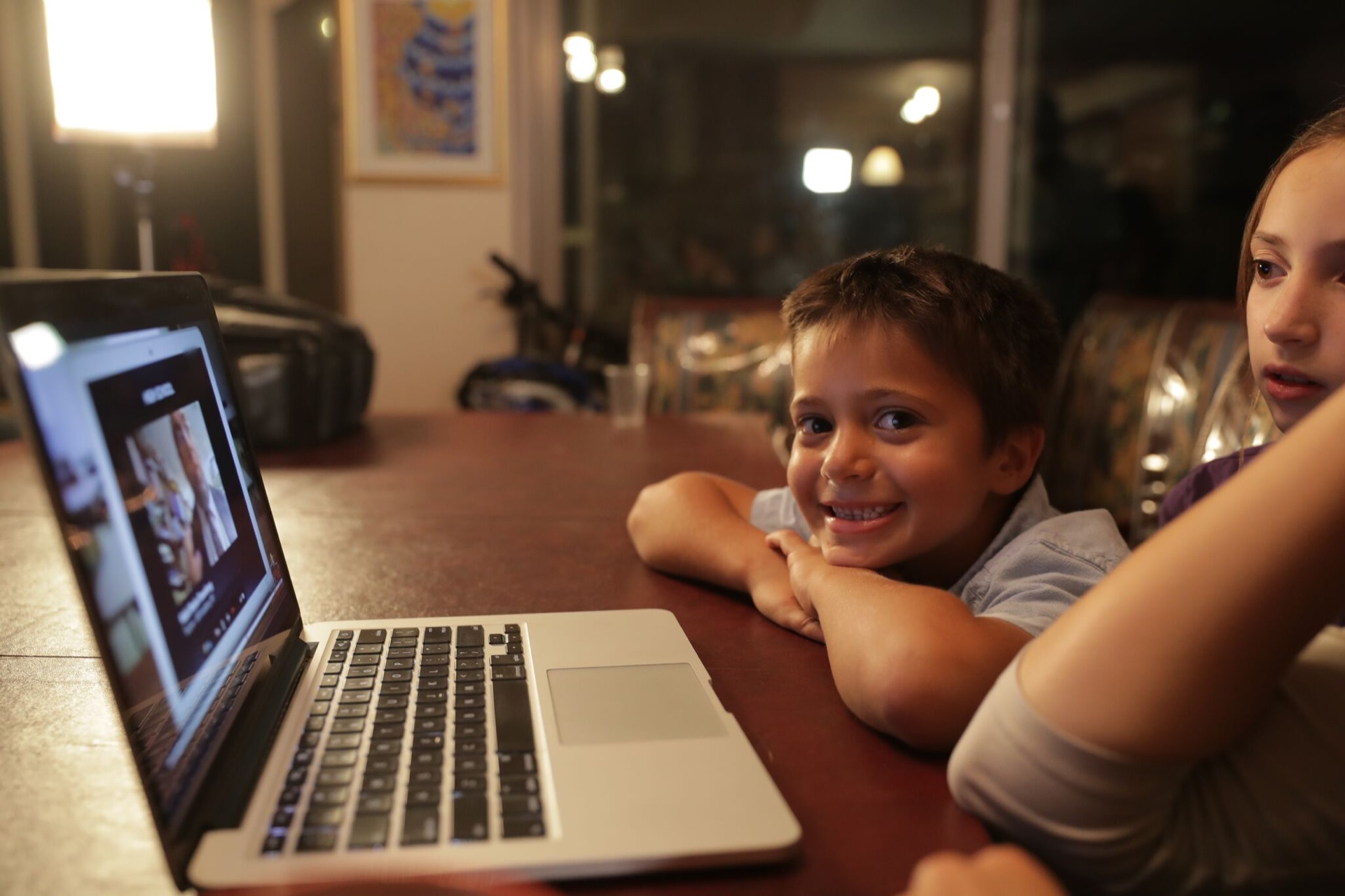 A boy smiling at a laptop in a warmly lit living room