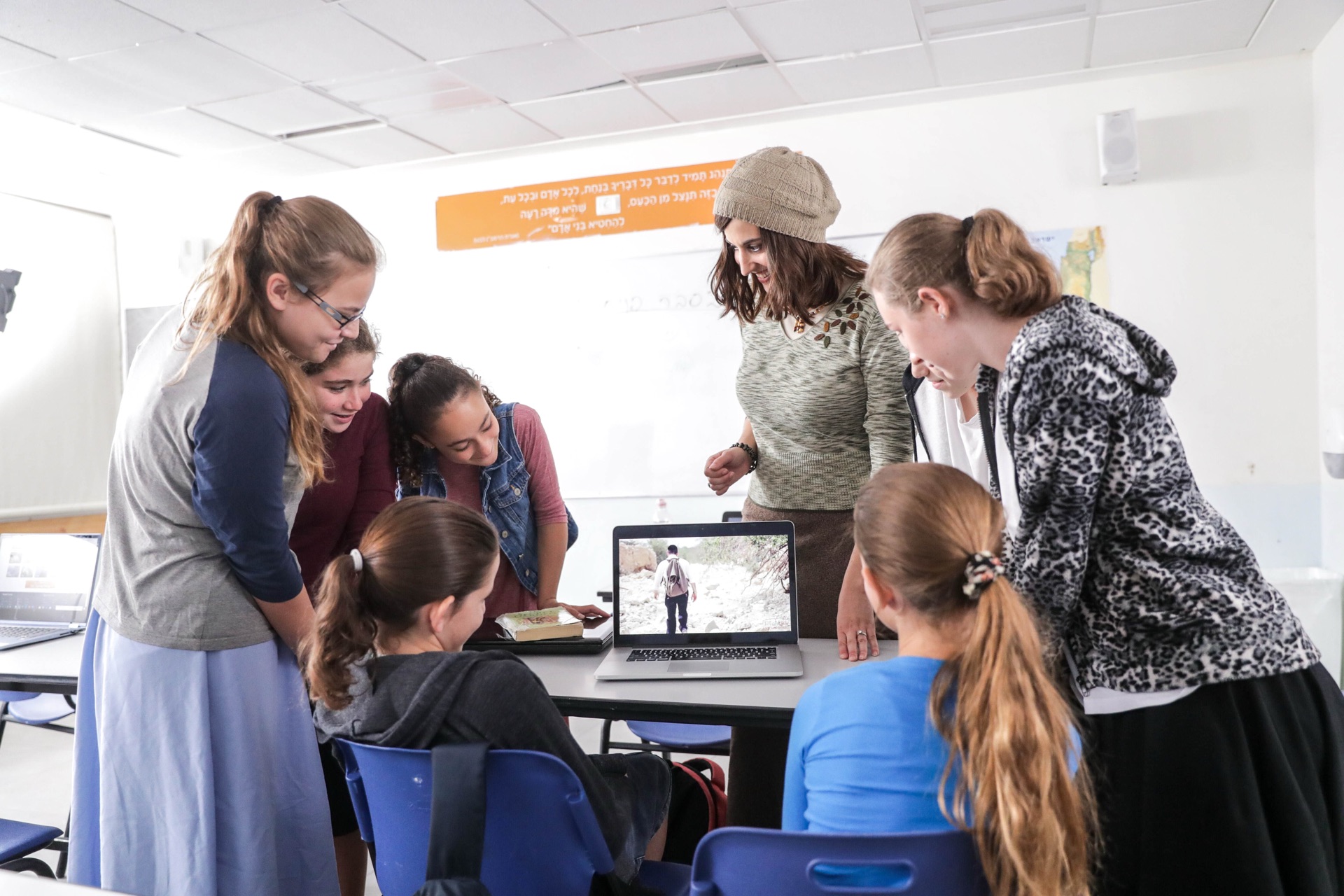 A classroom of girls gathered around a laptop with their teacher