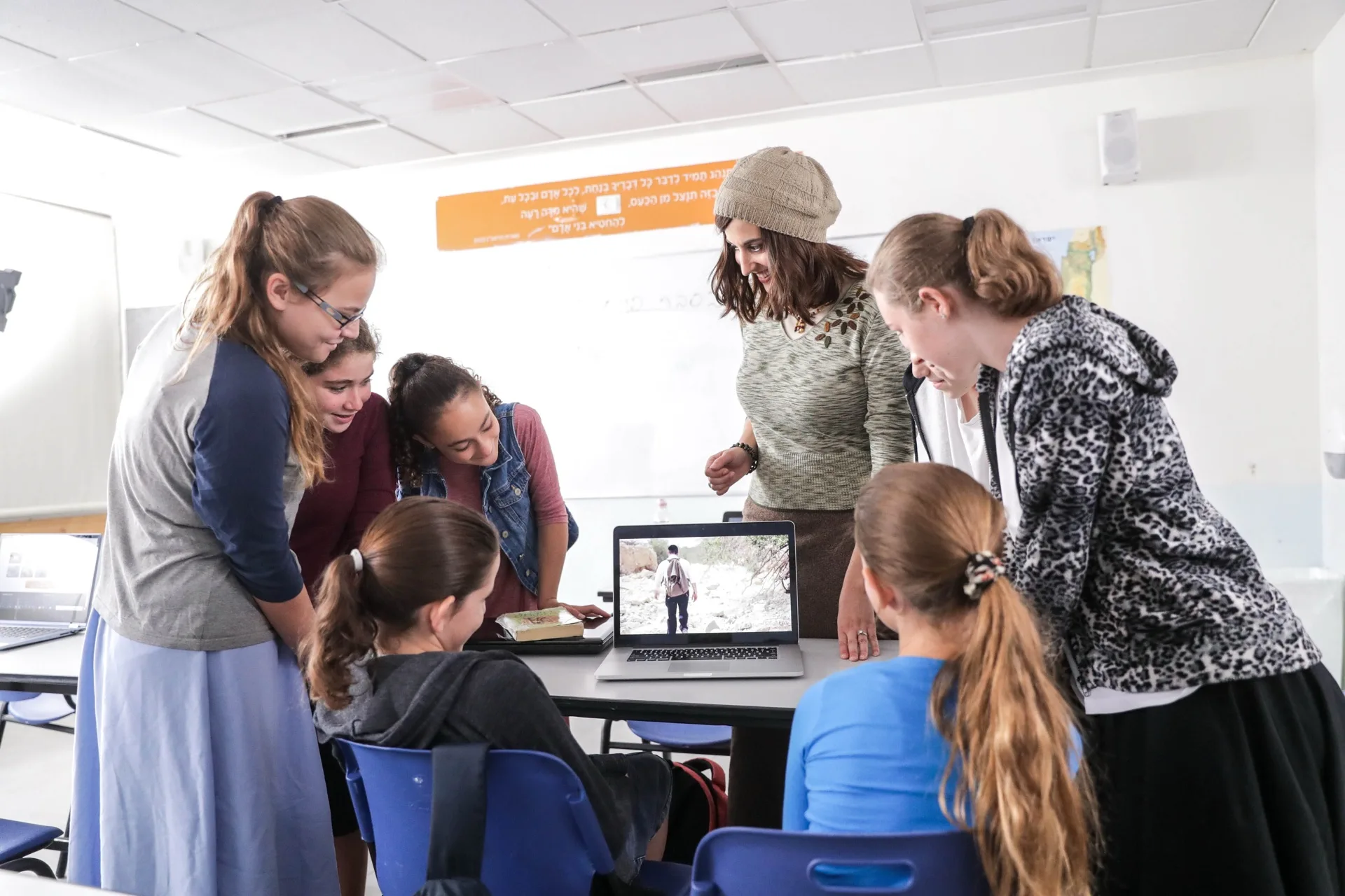 A teacher with a class of girls around a laptop