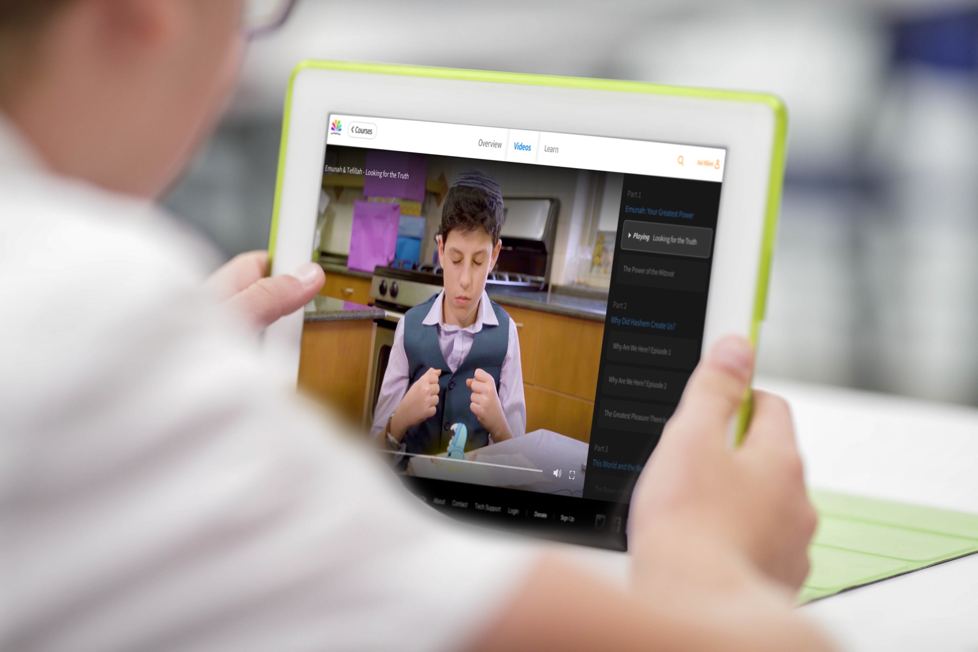 A child holding an iPad showing a Torah Live course page